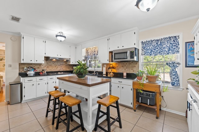 kitchen with appliances with stainless steel finishes, tasteful backsplash, white cabinetry, light tile patterned floors, and crown molding