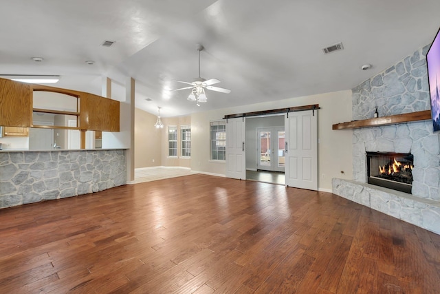 unfurnished living room featuring hardwood / wood-style flooring, ceiling fan, vaulted ceiling, a fireplace, and a barn door