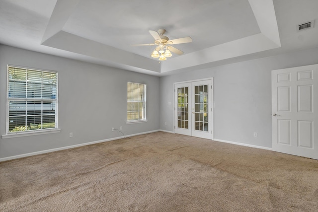 empty room featuring a raised ceiling, french doors, ceiling fan, and carpet floors