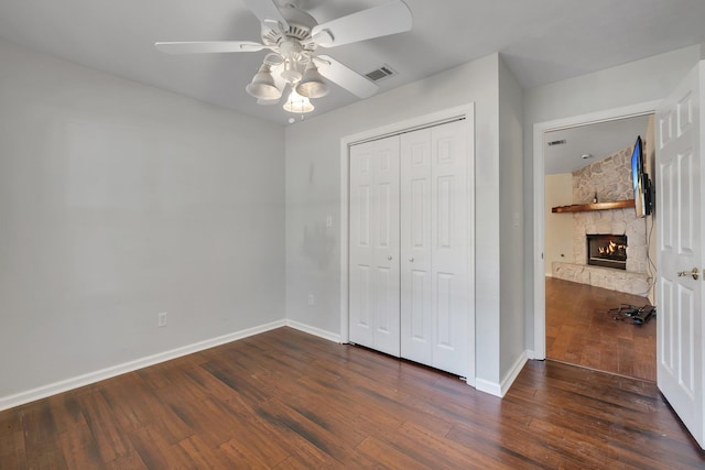 unfurnished bedroom with ceiling fan, a closet, dark hardwood / wood-style flooring, and a stone fireplace