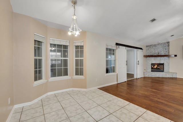 interior space featuring an inviting chandelier, a barn door, light hardwood / wood-style flooring, and a fireplace