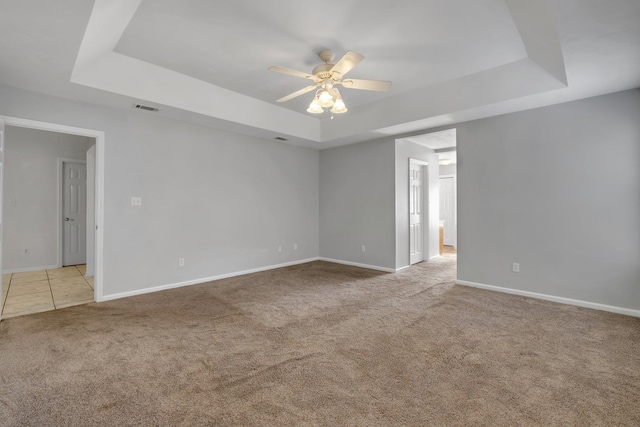 empty room featuring a raised ceiling, ceiling fan, and light colored carpet