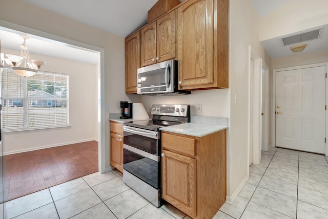 kitchen with appliances with stainless steel finishes, a notable chandelier, pendant lighting, and light tile patterned floors