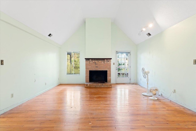 unfurnished living room with high vaulted ceiling, a fireplace, a wealth of natural light, and light hardwood / wood-style flooring