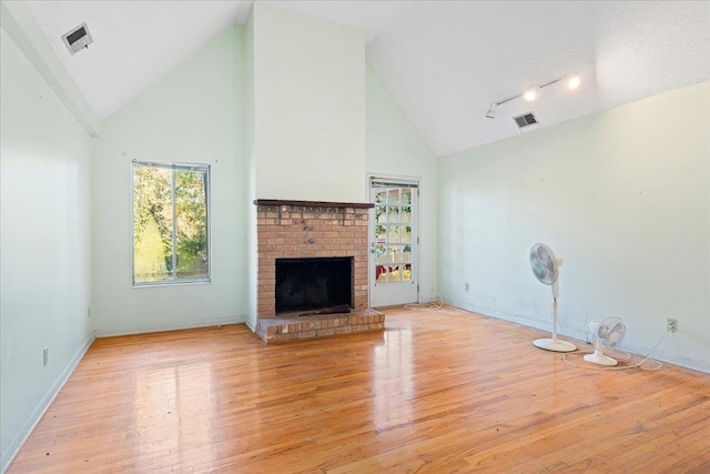 unfurnished living room featuring built in features, light wood-type flooring, high vaulted ceiling, and a brick fireplace