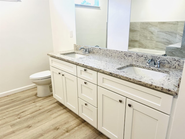 bathroom featuring wood finished floors, a sink, double vanity, and toilet