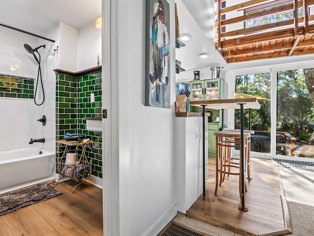 interior space with hardwood / wood-style floors, tile walls, and washtub / shower combination