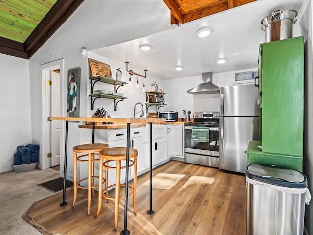 kitchen featuring butcher block counters, white cabinetry, wooden ceiling, wall chimney range hood, and appliances with stainless steel finishes