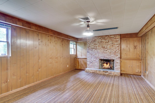 unfurnished living room with carpet flooring, a brick fireplace, and wood walls