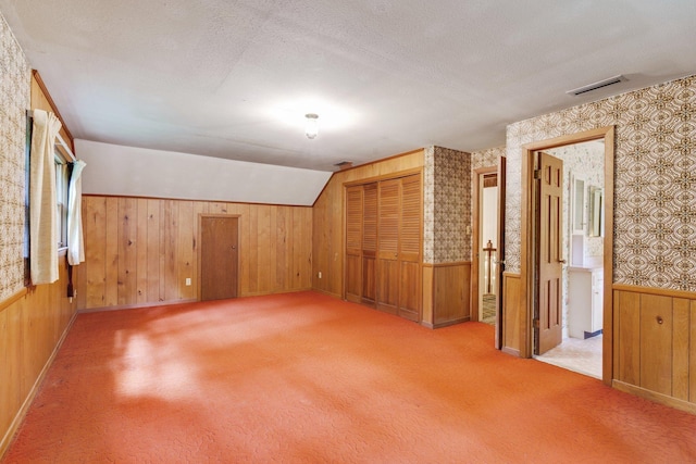 additional living space featuring carpet flooring, vaulted ceiling, a textured ceiling, and wood walls