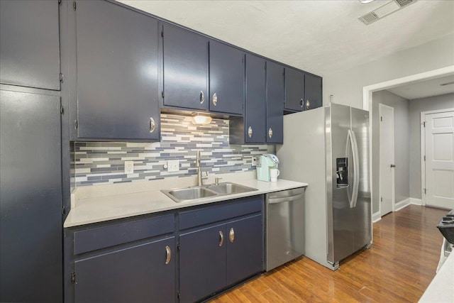 kitchen featuring appliances with stainless steel finishes, a sink, decorative backsplash, and wood finished floors
