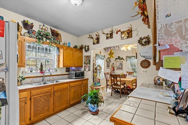 kitchen with light tile patterned floors, ceiling fan, a textured ceiling, tile countertops, and sink