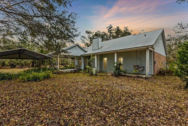 back house at dusk featuring a porch and a carport