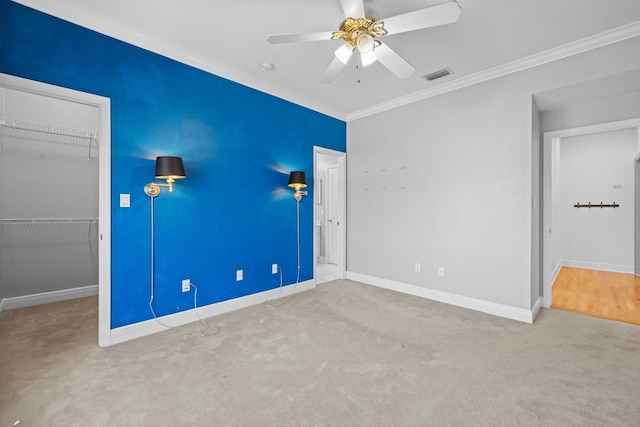 unfurnished bedroom featuring a closet, a walk in closet, carpet, crown molding, and ceiling fan