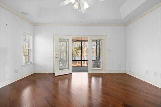 empty room featuring a tray ceiling, ceiling fan, dark hardwood / wood-style floors, and a wealth of natural light