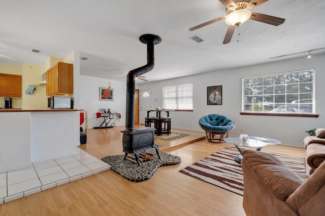 living room featuring a wood stove, track lighting, light hardwood / wood-style flooring, and ceiling fan