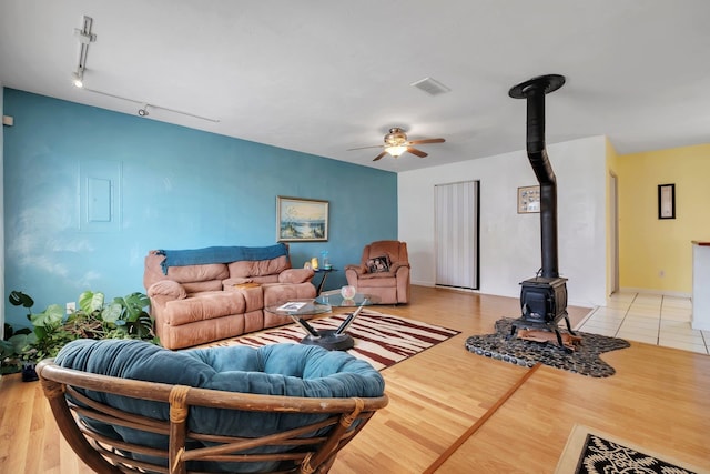 living room featuring ceiling fan, a wood stove, and light hardwood / wood-style floors