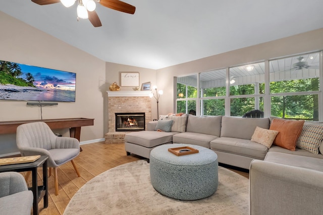living room featuring vaulted ceiling, a fireplace, light wood-type flooring, baseboards, and ceiling fan