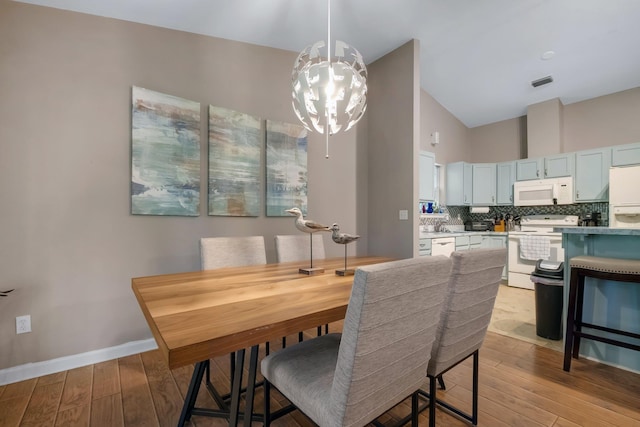 dining area featuring high vaulted ceiling, light wood-style flooring, visible vents, baseboards, and an inviting chandelier
