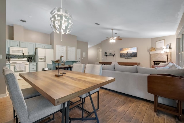 dining space with visible vents, a fireplace, ceiling fan, wood finished floors, and lofted ceiling