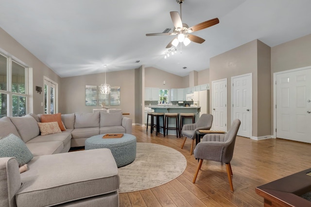 living area with a wealth of natural light, vaulted ceiling, light wood-style floors, and a ceiling fan