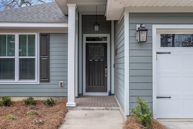 view of exterior entry featuring a shingled roof and a garage