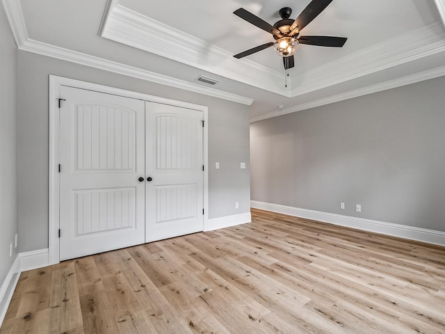 unfurnished bedroom featuring light hardwood / wood-style flooring, ceiling fan, a tray ceiling, ornamental molding, and a closet