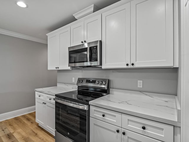 kitchen with ornamental molding, appliances with stainless steel finishes, white cabinets, and light stone counters