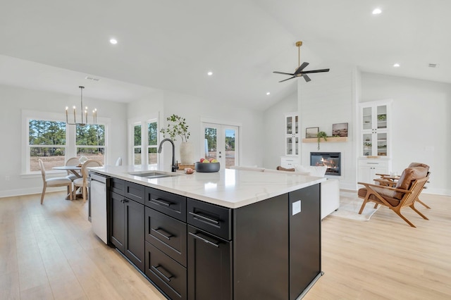 kitchen with sink, decorative light fixtures, stainless steel dishwasher, a fireplace, and a kitchen island with sink