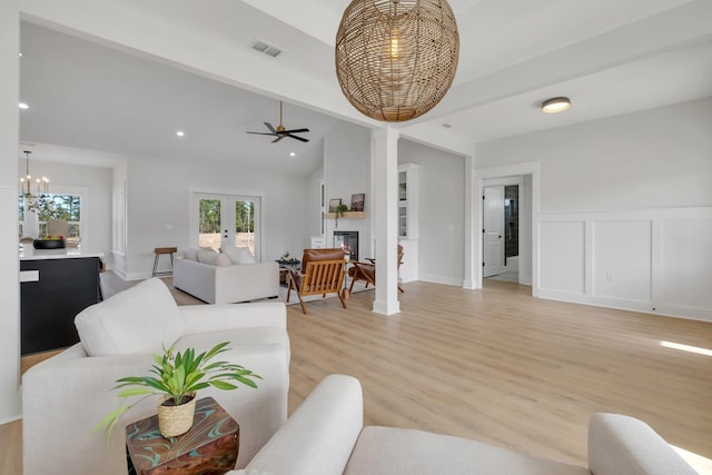 living room featuring lofted ceiling, ceiling fan with notable chandelier, french doors, and light wood-type flooring