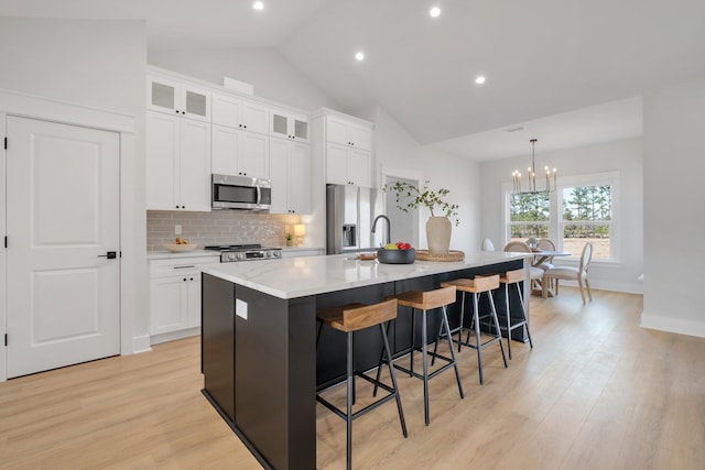 kitchen featuring white cabinetry, light hardwood / wood-style flooring, appliances with stainless steel finishes, an island with sink, and pendant lighting