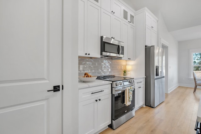 kitchen with appliances with stainless steel finishes, backsplash, light stone countertops, white cabinets, and light wood-type flooring