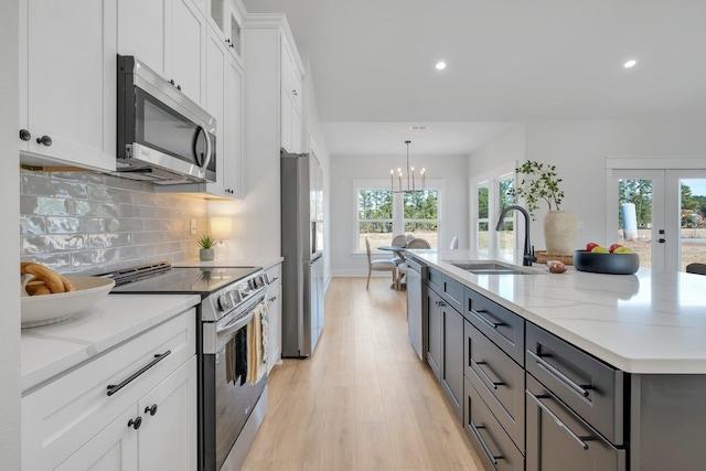 kitchen featuring pendant lighting, sink, stainless steel appliances, light stone countertops, and white cabinets