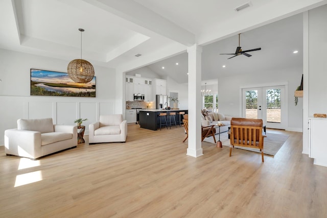 living room featuring a tray ceiling, lofted ceiling with beams, ceiling fan with notable chandelier, french doors, and light wood-type flooring