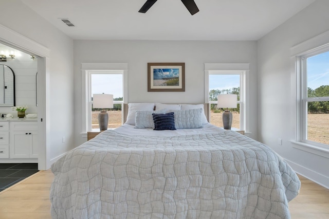 bedroom with ceiling fan, ensuite bath, multiple windows, and light wood-type flooring