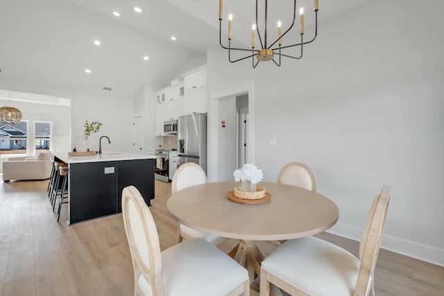 dining room featuring an inviting chandelier, sink, light hardwood / wood-style floors, and high vaulted ceiling