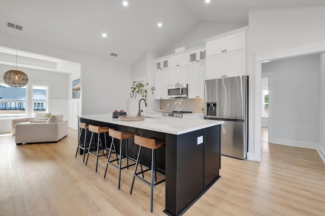 kitchen featuring pendant lighting, white cabinetry, a kitchen island with sink, stainless steel appliances, and light stone counters