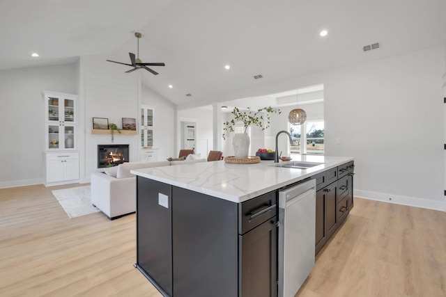 kitchen featuring sink, dishwasher, a kitchen island with sink, light hardwood / wood-style floors, and a large fireplace