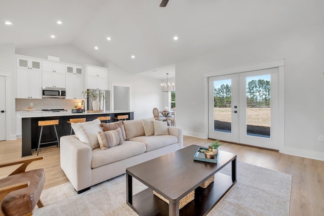 living room with high vaulted ceiling, sink, light wood-type flooring, and french doors