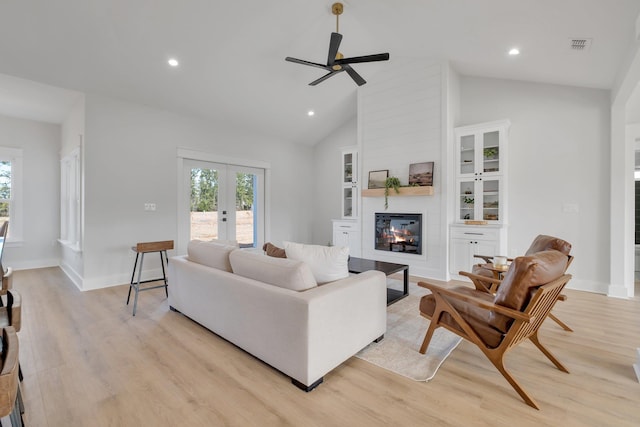 living room with french doors, a large fireplace, a healthy amount of sunlight, and light wood-type flooring