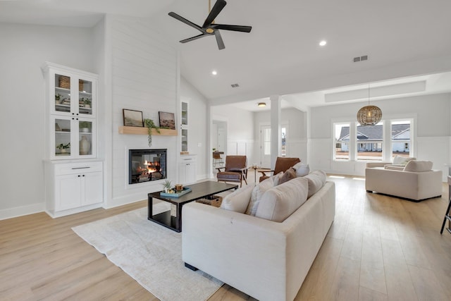 living room featuring high vaulted ceiling, a large fireplace, ceiling fan, and light hardwood / wood-style flooring