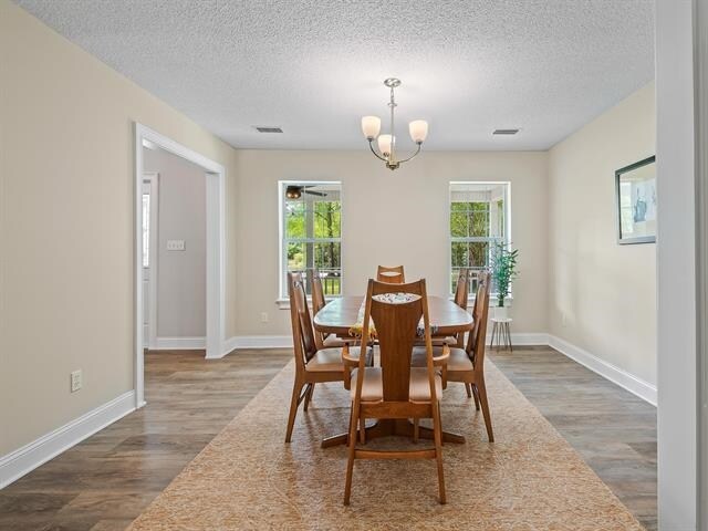 dining space featuring dark wood-type flooring, a textured ceiling, and a notable chandelier