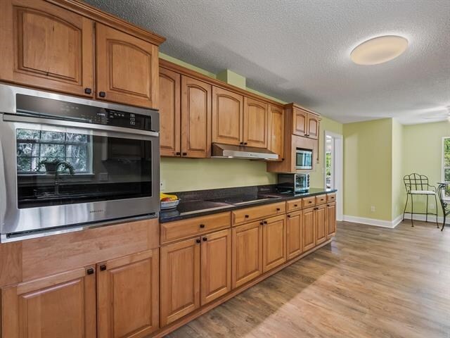 kitchen with stainless steel appliances, a textured ceiling, and light hardwood / wood-style flooring