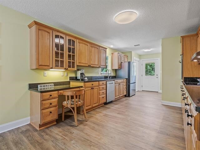 kitchen featuring appliances with stainless steel finishes, a textured ceiling, built in desk, and light hardwood / wood-style floors