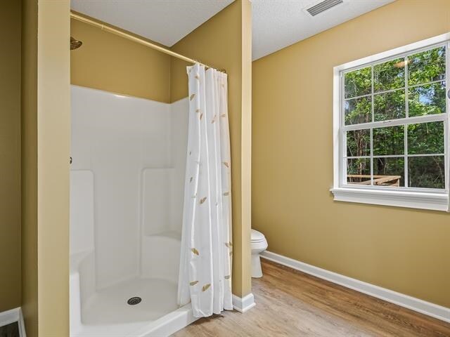 bathroom featuring walk in shower, plenty of natural light, hardwood / wood-style flooring, and toilet