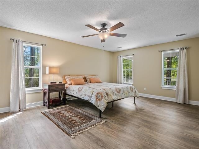 bedroom featuring ceiling fan, multiple windows, a textured ceiling, and wood-type flooring