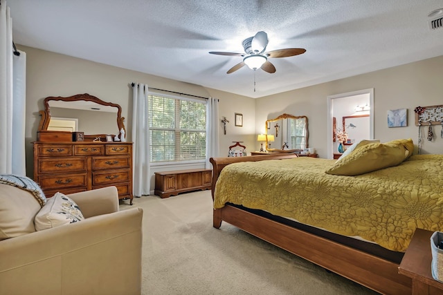 bedroom featuring a textured ceiling, light colored carpet, ensuite bath, and ceiling fan