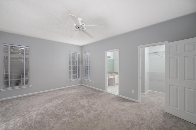 unfurnished bedroom with ensuite bath, light colored carpet, ceiling fan, a closet, and a spacious closet