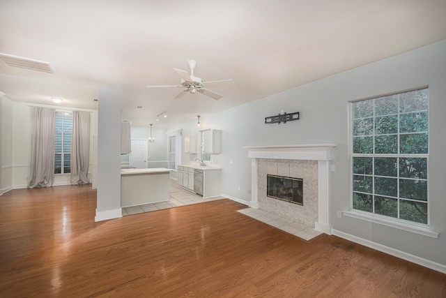 unfurnished living room featuring ceiling fan, a wealth of natural light, a tiled fireplace, and light wood-type flooring