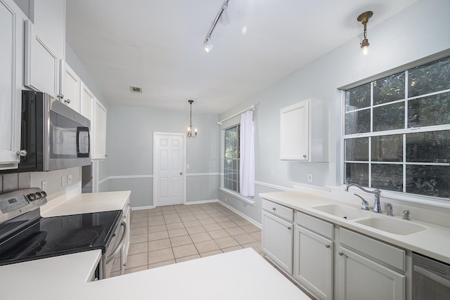 kitchen with stainless steel appliances, light tile patterned floors, hanging light fixtures, sink, and white cabinets